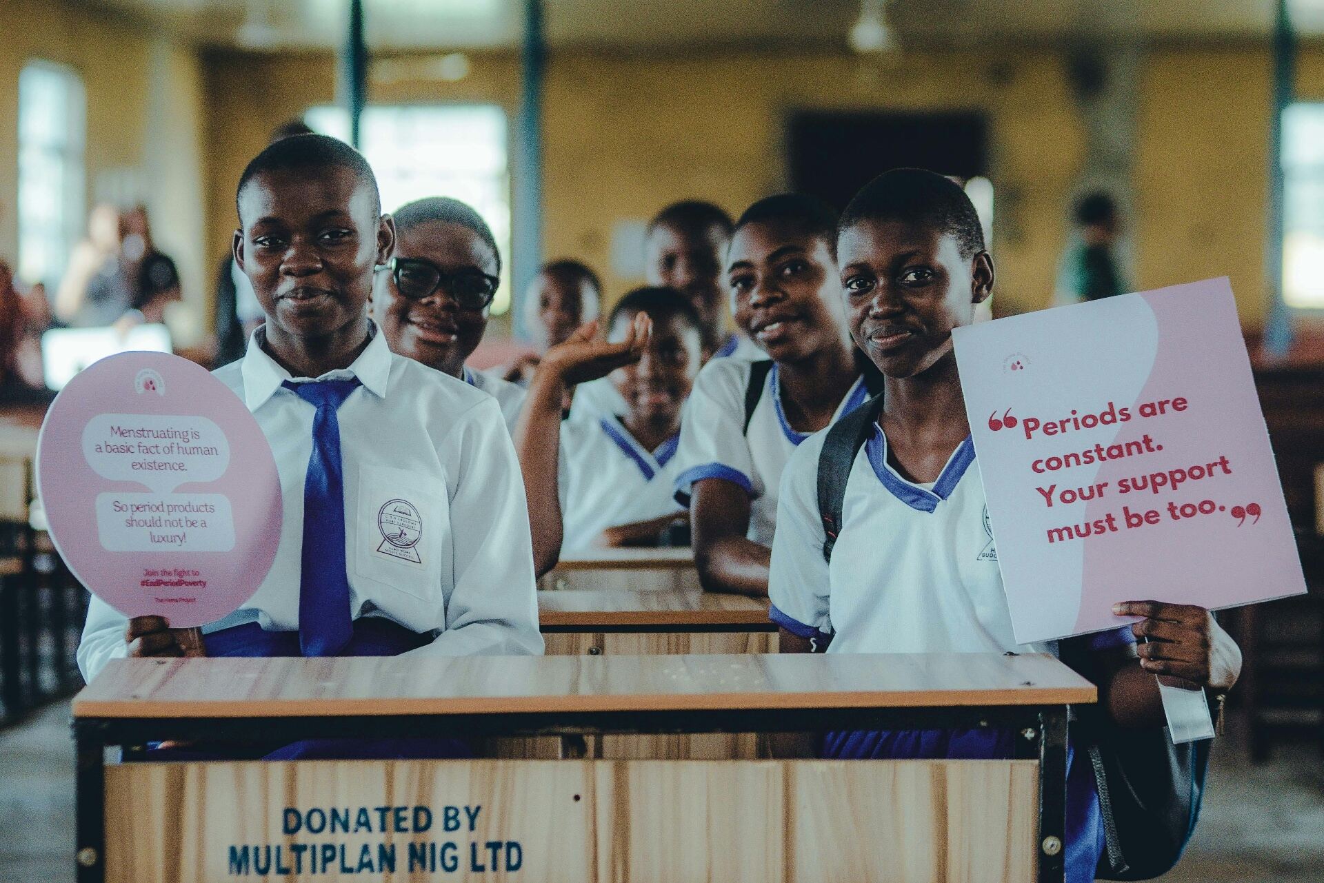 Students seated at a donated school desk holding awareness signs